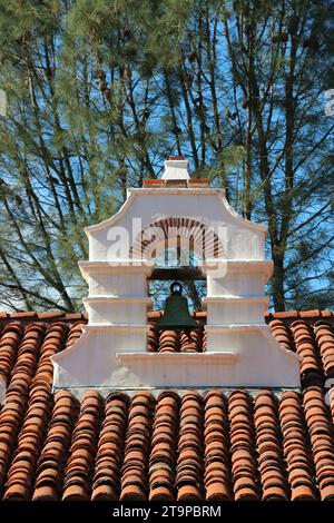 Campana singola, intemprata, sospesa in una torre bianca in adobe sul tetto piastrellato della guest House, Mission San Antonio de Padova. Foto Stock