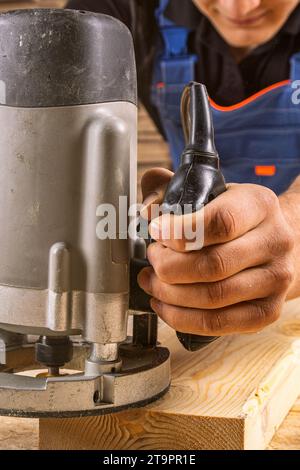 Un forte falegname maschile in abiti da lavoro lavora e sega con entusiasmo un asse di legno su un tavolo di legno in un'officina industriale Foto Stock