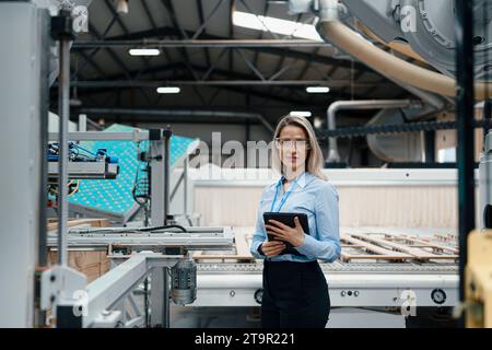 Ingegnere donna in piedi in una moderna fabbrica industriale. Impianto di produzione con robotica e automazione. Leader femminile, CEO nell'industria pesante Foto Stock