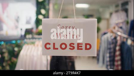 Il negozio di abbigliamento alla moda è chiuso di notte dopo aver terminato l'orario di lavoro. Primo piano estremo su Sorry we are CLOSED message sign on fashion boutique door in Mall at shift end Foto Stock