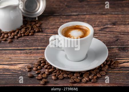 Espresso macchiato in una tazza di porcellana bianca con latte e chicchi di caffè su un tavolo di legno Foto Stock