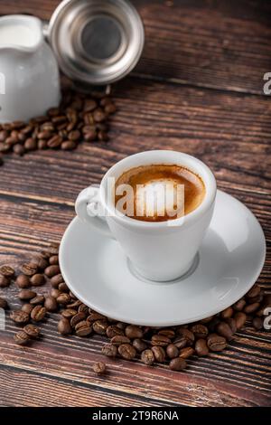 Espresso macchiato in una tazza di porcellana bianca con latte e chicchi di caffè su un tavolo di legno Foto Stock