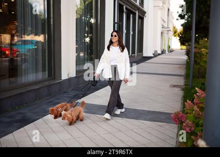 Una donna cammina per la strada cittadina con due cani di piccola taglia al guinzaglio. Animali domestici e persone. Foto Stock