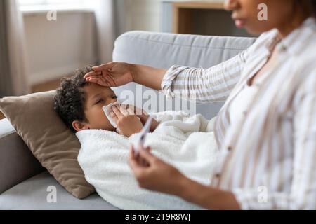 Influenza stagionale. Mamma Nera preoccupata a controllare la temperatura di figlio malato a casa Foto Stock