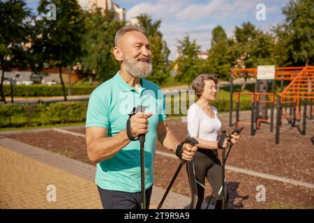 Felice coppia in pensione che si sta allenando con il Pole Walk in un parco urbano Foto Stock
