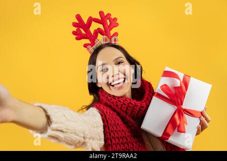 lady che tiene il regalo di Capodanno che fa selfie su sfondo giallo Foto Stock