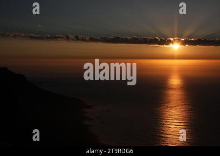 Il sole che tramonta si apre dietro le nuvole sopra l'oceano Altantic. Foto Stock