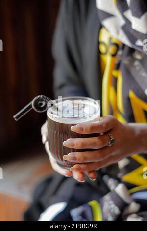 Primo piano di una mano femminile che tiene un bicchiere di caffè con cubetti di ghiaccio Foto Stock