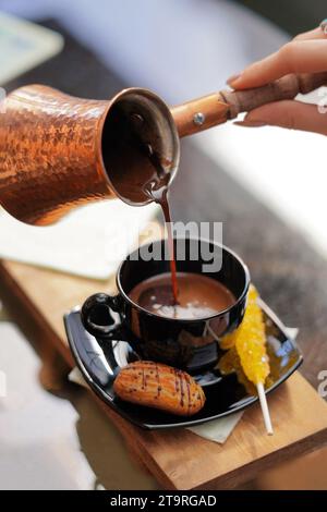 Caffè versato da una caffettiera turca in rame in una tazza da caffè nera. Foto Stock