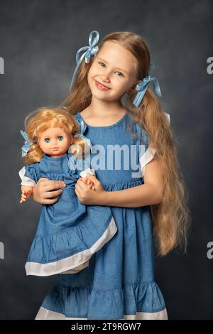 Ritratto di bambino di?ute girl e bambola isolato su sfondo grigio. Bambino e giocattolo preferito. Un regalo per un compleanno o un'altra vacanza. Foto Stock