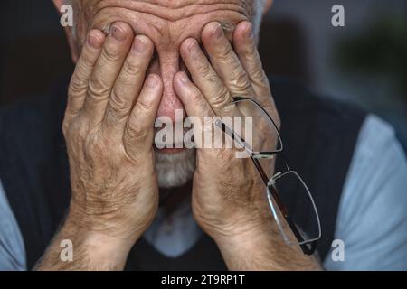 L'uomo anziano depresso si è coperto il viso con entrambe le mani Foto Stock