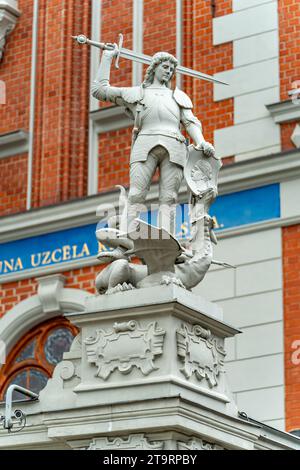 Una statua di un cavaliere vittorioso in cima a un drago sconfitto di fronte a un edificio a riga, in Lettonia Foto Stock