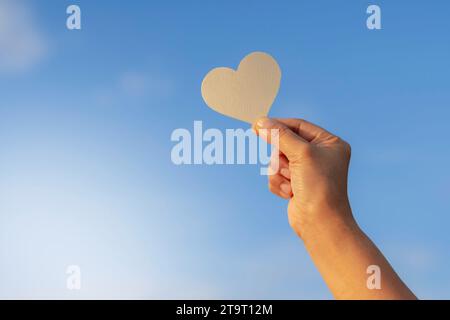 La mano di una donna regge un pezzo di carta a forma di cuore. Su nel cielo a San Valentino Foto Stock