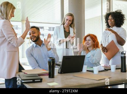 Colleghi multietnici che sorridono e celebrano il successo mentre lavorano in ufficio. Concetto aziendale. Foto Stock