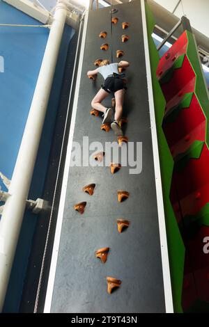 Bambina di nove anni / bambina di 9 anni su una parete da arrampicata interna, con corda di sicurezza in caso di caduta, in un centro sportivo. REGNO UNITO. (136) Foto Stock