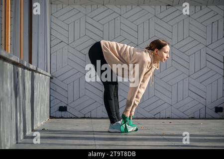Una giovane atleta esegue esercizi di stretching per i muscoli della schiena e delle gambe con una cintura fitness, allenandosi con abbigliamento sportivo mentre si sta in piedi su una p di legno Foto Stock