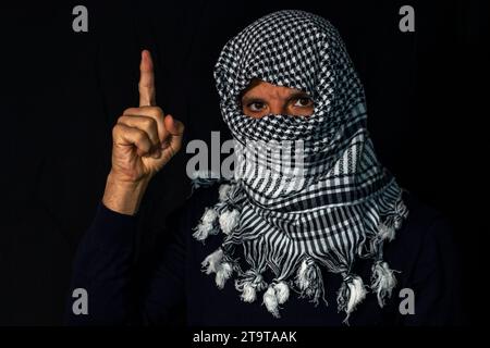 Uomo adulto con sciarpa palestinese messo sulla testa su uno sfondo nero che regge una bandiera di Israele Foto Stock