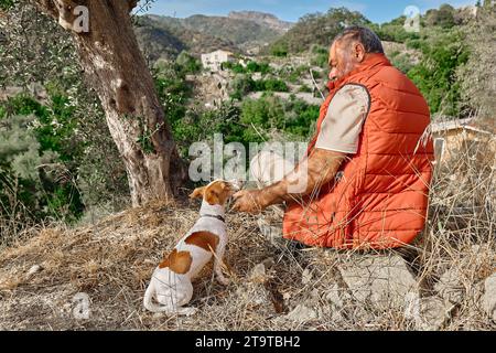 Uomo dai capelli grigi con il suo piccolo e carino Jack Russell Terrier che cammina all'aperto contro la natura panoramica delle montagne. Foto Stock