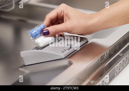 la mano femminile inserisce il tablet lavastoviglie nella lavastoviglie automatica. Primo piano Foto Stock