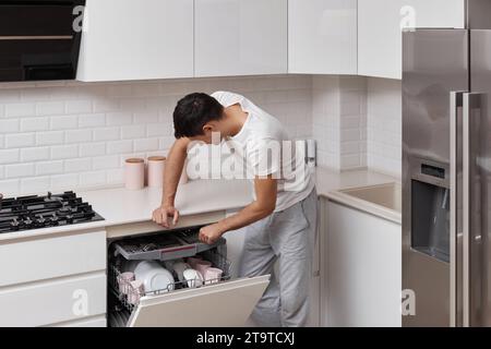 bell'uomo positivo che mette piatti in lavastoviglie in cucina Foto Stock