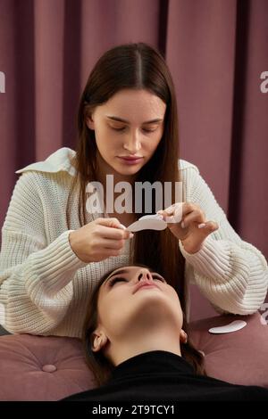 cosmetologo che prepara il nastro adesivo sotto gli occhi. Procedura di estensione ciglia Foto Stock