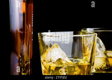 whisky con ghiaccio nei bicchieri davanti alla bottiglia su sfondo nero, con riflesso Foto Stock