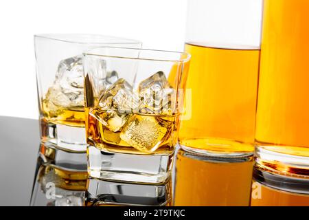 due bicchieri di whisky vicino a bottiglie su fondo nero con riflesso, tempo di relax con whisky Foto Stock