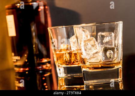 due bicchieri di whisky davanti alla bottiglia di whisky su un tavolo nero con riflessi e atmosfera calda Foto Stock