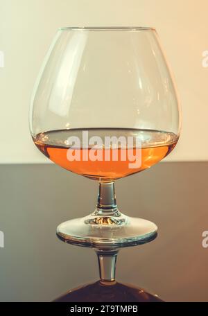 snifter di brandy in un elegante tipico bicchiere di cognac su sfondo chiaro, con riflesso Foto Stock