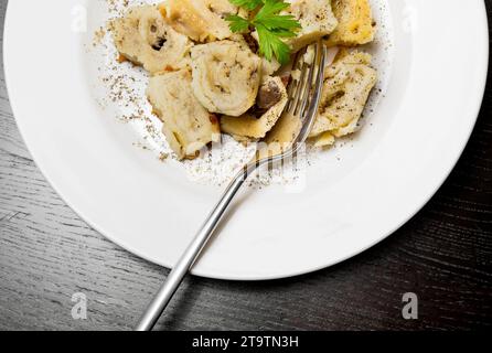 vista dall'alto del piatto di pasta italiana con funghi porcini e salsa besciamella con pepe vicino alla forchetta sul tavolo nero Foto Stock