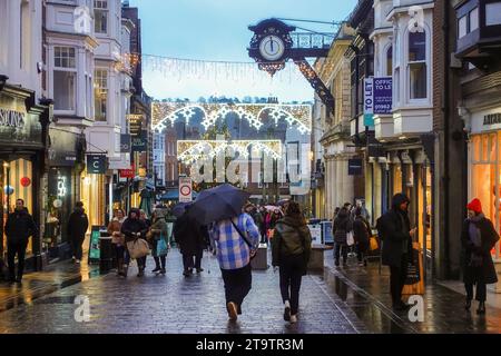 Gli amanti dello shopping passeggiano lungo Winchester High Street in inverno con decorazioni natalizie e alberi, Hampshire, Inghilterra, Regno Unito Foto Stock