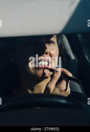 donna di 40 anni che applica il trucco nello specchietto retrovisore della vettura. Foto Stock