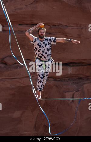 Un uomo in costume che cammina su una linea alta che mette un pompelmo sulla testa al GGBY World Highline Festival. Moab, Utah. Foto Stock