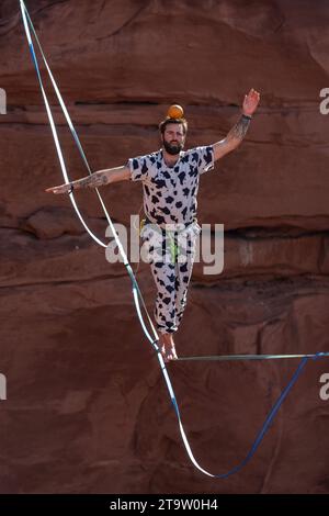 Un uomo in costume che cammina su una linea alta con un pompelmo bilanciato sulla testa al GGBY World Highline Festival. Moab, Utah. Foto Stock