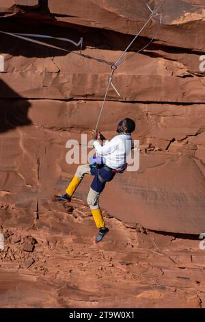 Un Highliner maschile che indossa una benda perde l'equilibrio e fruste, o cade fuori dall'alto in un festival Highline nello Utah. Imbracatura protettiva HIS e. Foto Stock