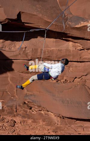 Un Highliner maschile che indossa una benda perde l'equilibrio e fruste, o cade fuori dall'alto in un festival Highline nello Utah. Imbracatura protettiva HIS e. Foto Stock