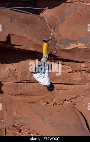 Un Highliner maschile che indossa una benda perde l'equilibrio e fruste, o cade fuori dall'alto in un festival Highline nello Utah. Imbracatura protettiva HIS e. Foto Stock