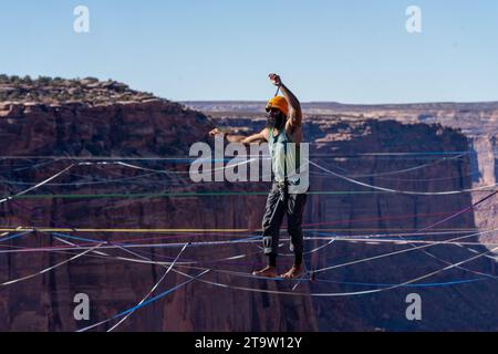 Vista teleobiettivo di un uomo che cammina su una linea principale al GGBY World Highline Festival nel Mineral Canyon vicino a Moab, Utah. Foto Stock