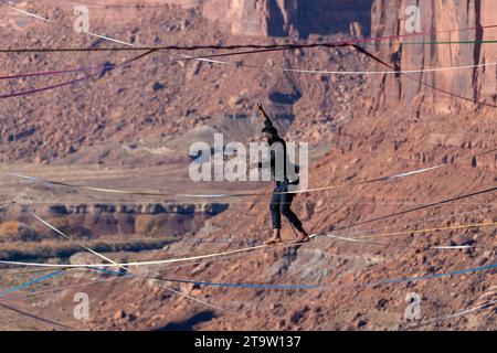 Vista teleobiettivo di un uomo che cammina su una linea principale al GGBY World Highline Festival nel Mineral Canyon vicino a Moab, Utah. Foto Stock