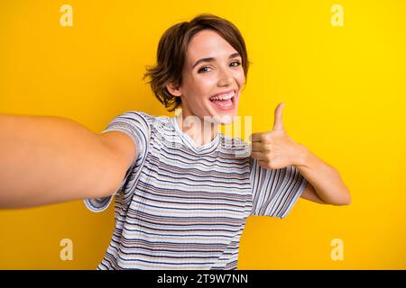 Foto di una ragazza blogger felice positiva vestita con abiti eleganti che mostrano il pollice in alto isolato su sfondo di colore giallo Foto Stock