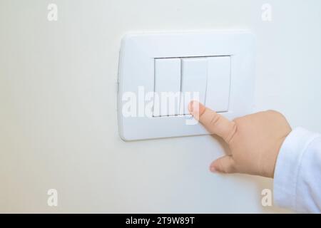 adorabile bambino che accende l'interruttore di luce bianca con il dito della mano, il concetto di nuova generazione e la vista ravvicinata Foto Stock