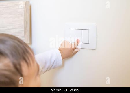 adorabile bambino che accende l'interruttore di luce bianca con il dito della mano Foto Stock