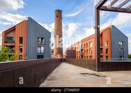 Passerella deserta che conduce a due moderni edifici di appartamenti sovrastati da una vecchia torre in mattoni in una soleggiata giornata estiva Foto Stock