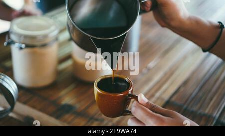 Il barista versa il caffè in tazza messo sul tavolo, pavimento in bambù. Parte centrale della donna che versa il caffè in una tazza. Stile thailandese locale. Foto Stock