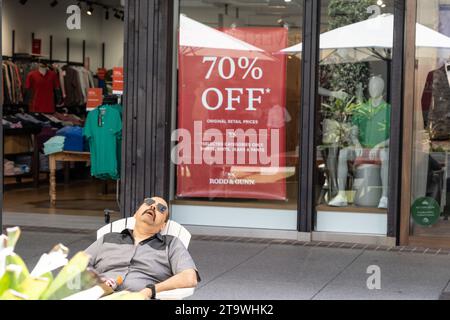 Surfers Paradise Australia - 21 settembre 2023; l'uomo si addormenta in una sedia all'aperto nella vetrina del negozio di fronte e un cartello sconto che attende la moglie dello shopping Foto Stock