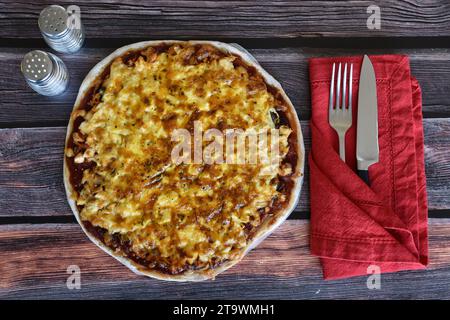 Pizza fresca fatta in casa servita su un tavolo di legno. Pizza di pollo con formaggio. Tovagliolo rosso, posate, coltello e forchetta, agitatori con sale e pepe. Vista dall'alto. Foto Stock