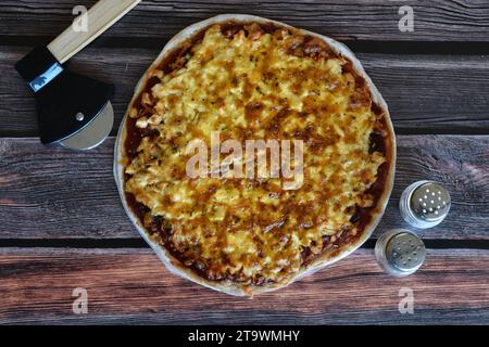 Pizza fresca fatta in casa servita su un tavolo rustico in legno. Deliziosa pizza di pollo con formaggio. Tritatutto per pizza, agitatori per sale e pepe. Vista dall'alto. Foto Stock