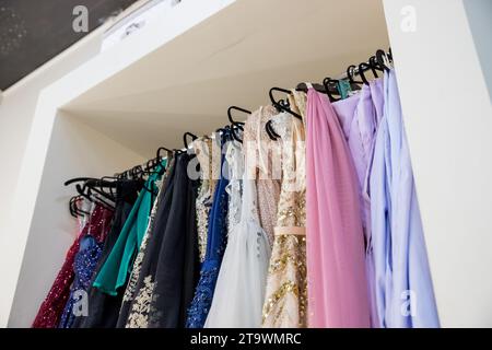 Abiti da sera diversi su appendiabiti in boutique. Abiti di lusso con paillettes rosa, blu e grigio per donna appesi a grucce. Una fila di diversi abiti Foto Stock