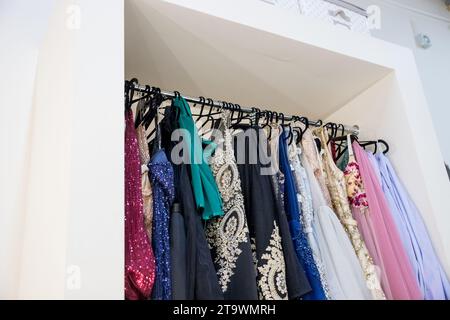 Abiti da sera diversi su appendiabiti in boutique. Abiti di lusso con paillettes rosa, blu e grigio per donna appesi a grucce. Una fila di diversi abiti Foto Stock