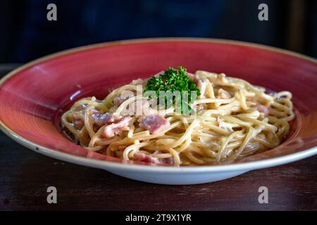 una carbonara di spaghetti appena preparata servita in una ciotola rossa. Foto Stock